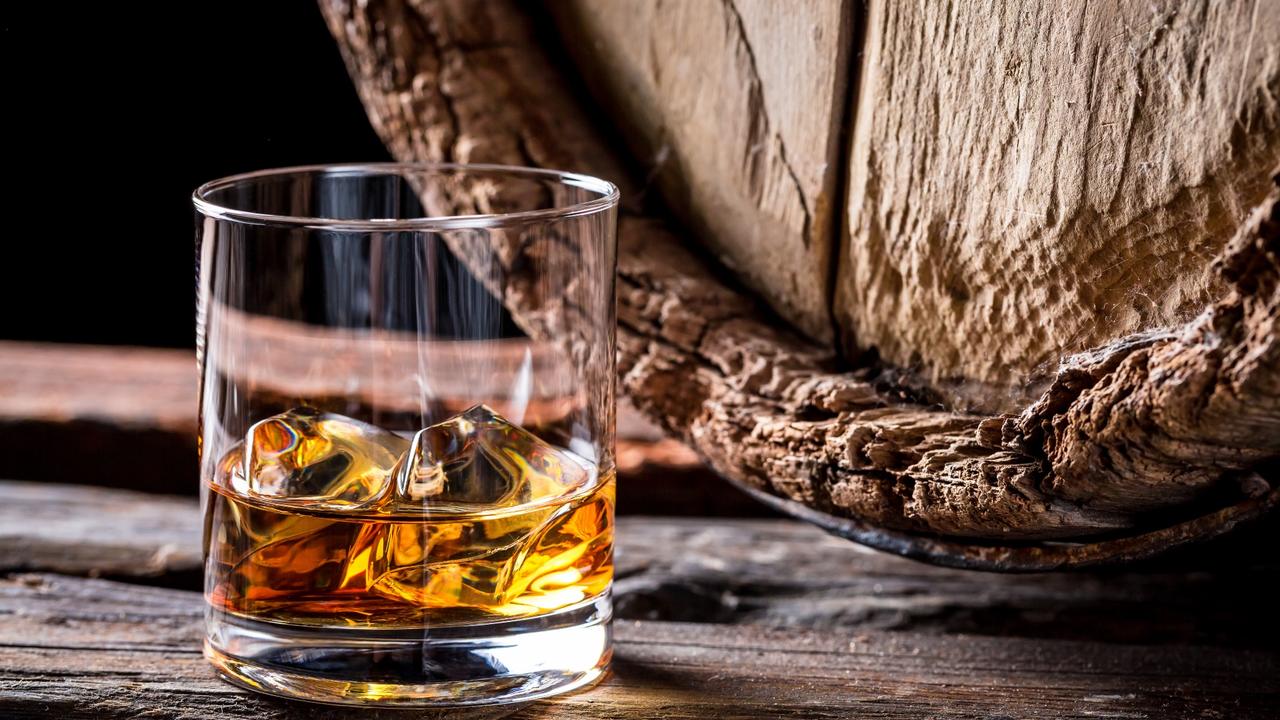 Glass of Scotch whiskey next to an oak barrel. 